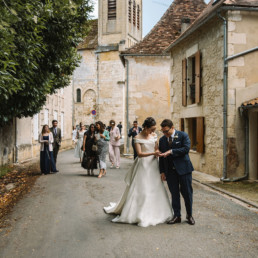 Bride and groom stopping in the street of quaint stone house village on way back from church for groom to admire bride's ring. Guests in background making way back to the Aristocratic chateau wedding venue in the Dordogne