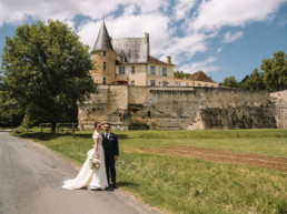 Couple standing in front of French Aristocratic Chateau wedding venue in the Dordogne perched high above behind them on a rocky outcrop