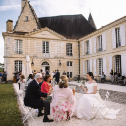 Bride sitting at occasional table with two guest chatting on courtyard of Aristocratic chateau wedding venue in the Dordogne