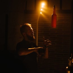 Flair cocktail barman juggling bottles into air in darken bar